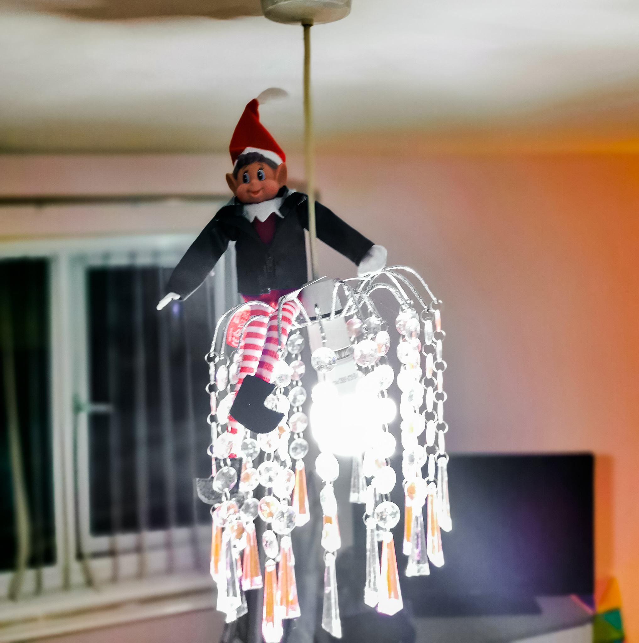 an elf in a black leather jacket swinging of an acrylic droplet lightshade