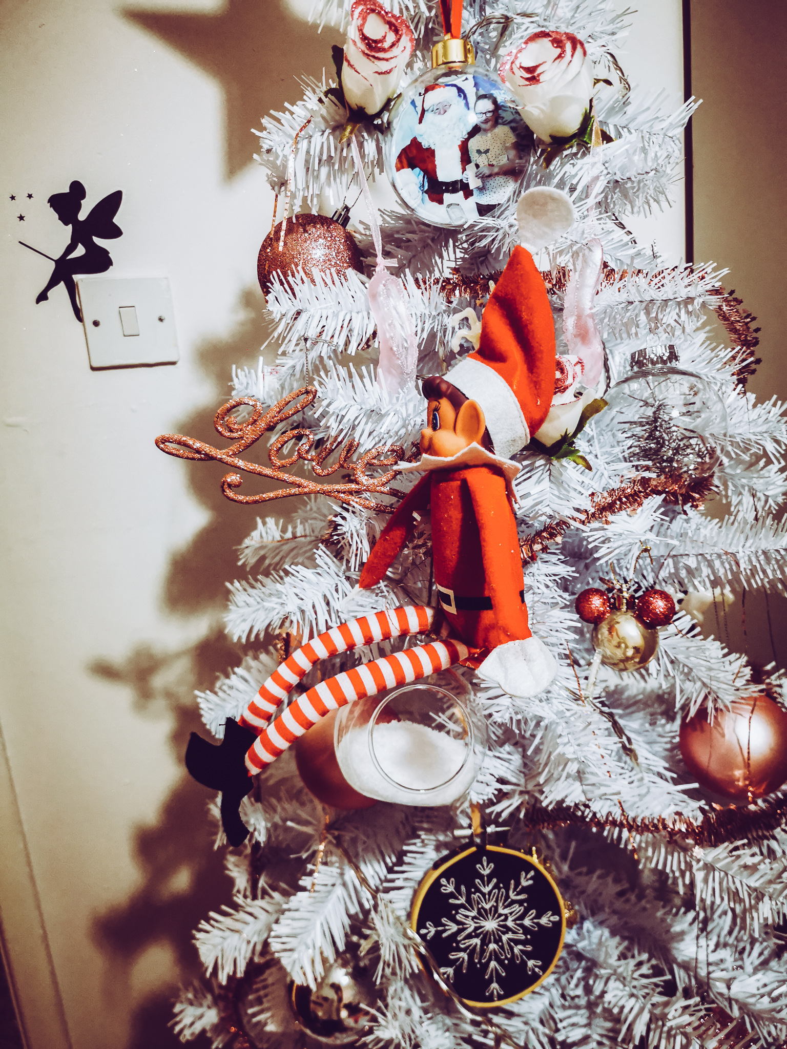 an elf sitting on top of a bauble on a white christmas tree