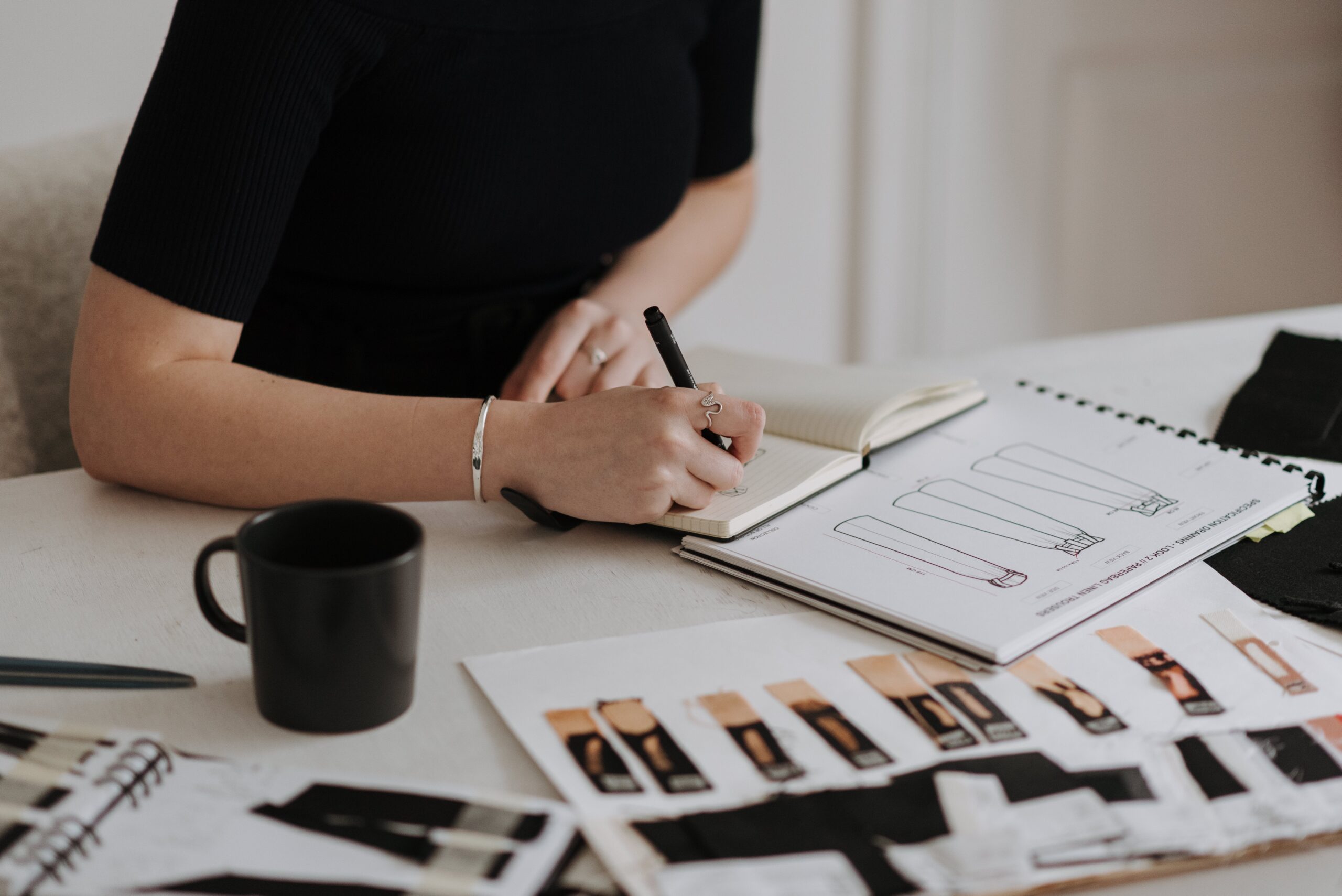person writing in a pad on a desk with business manuals