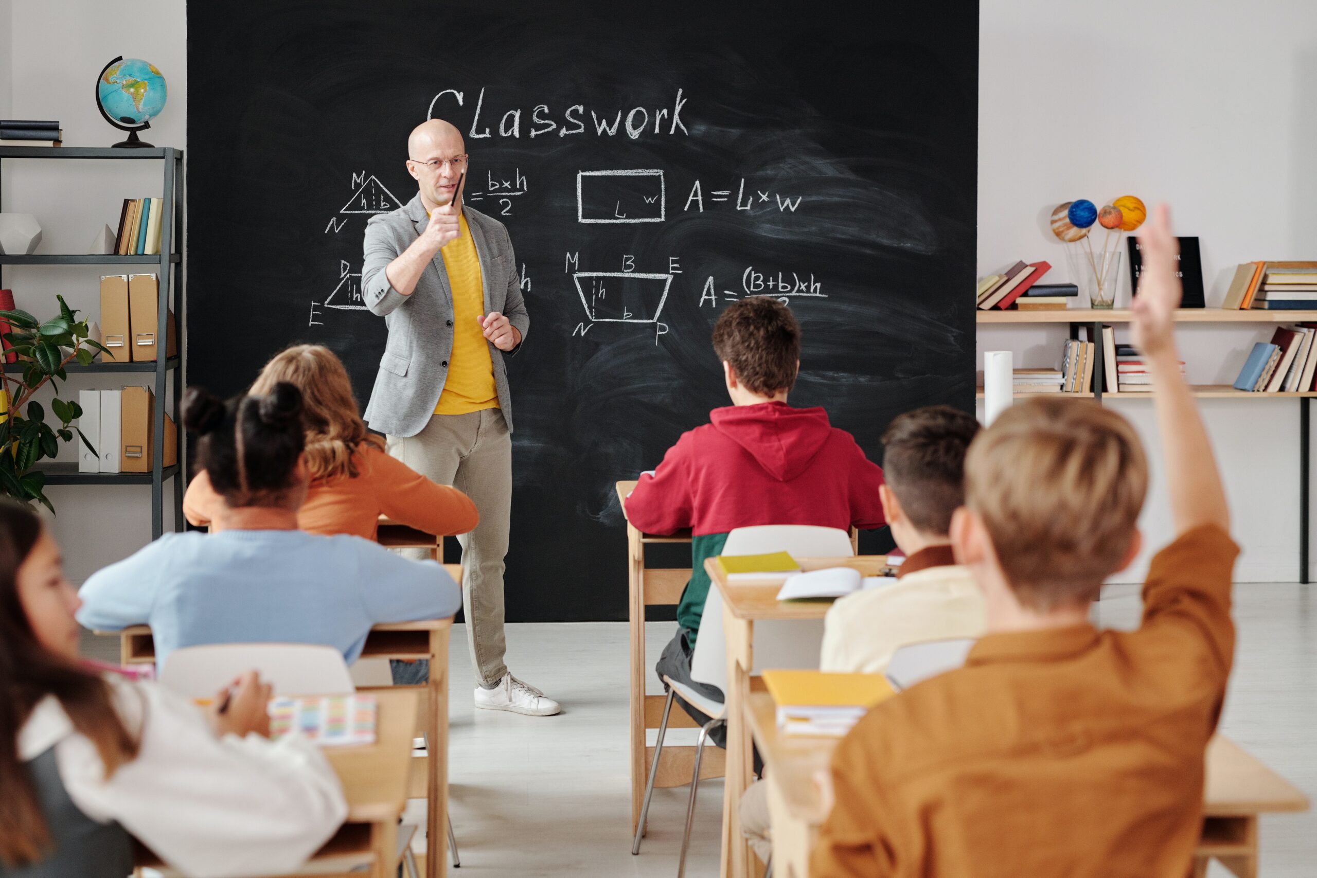 male teacher standing in front of a blackboard in front of a class of students