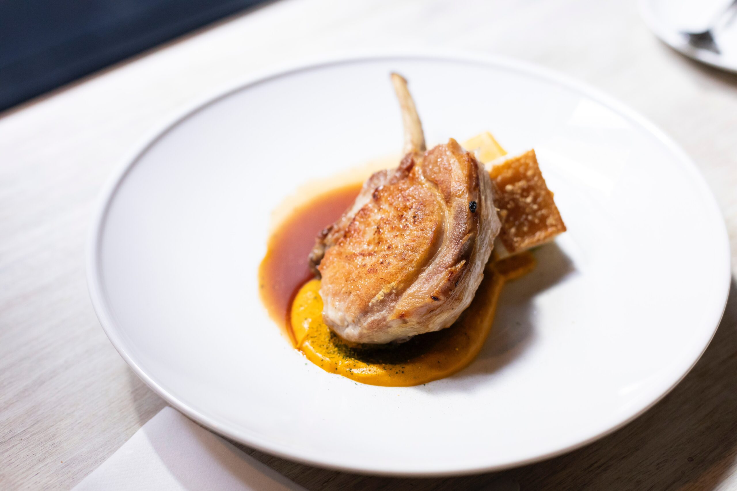 white plate with a small cut of lamb on the bone