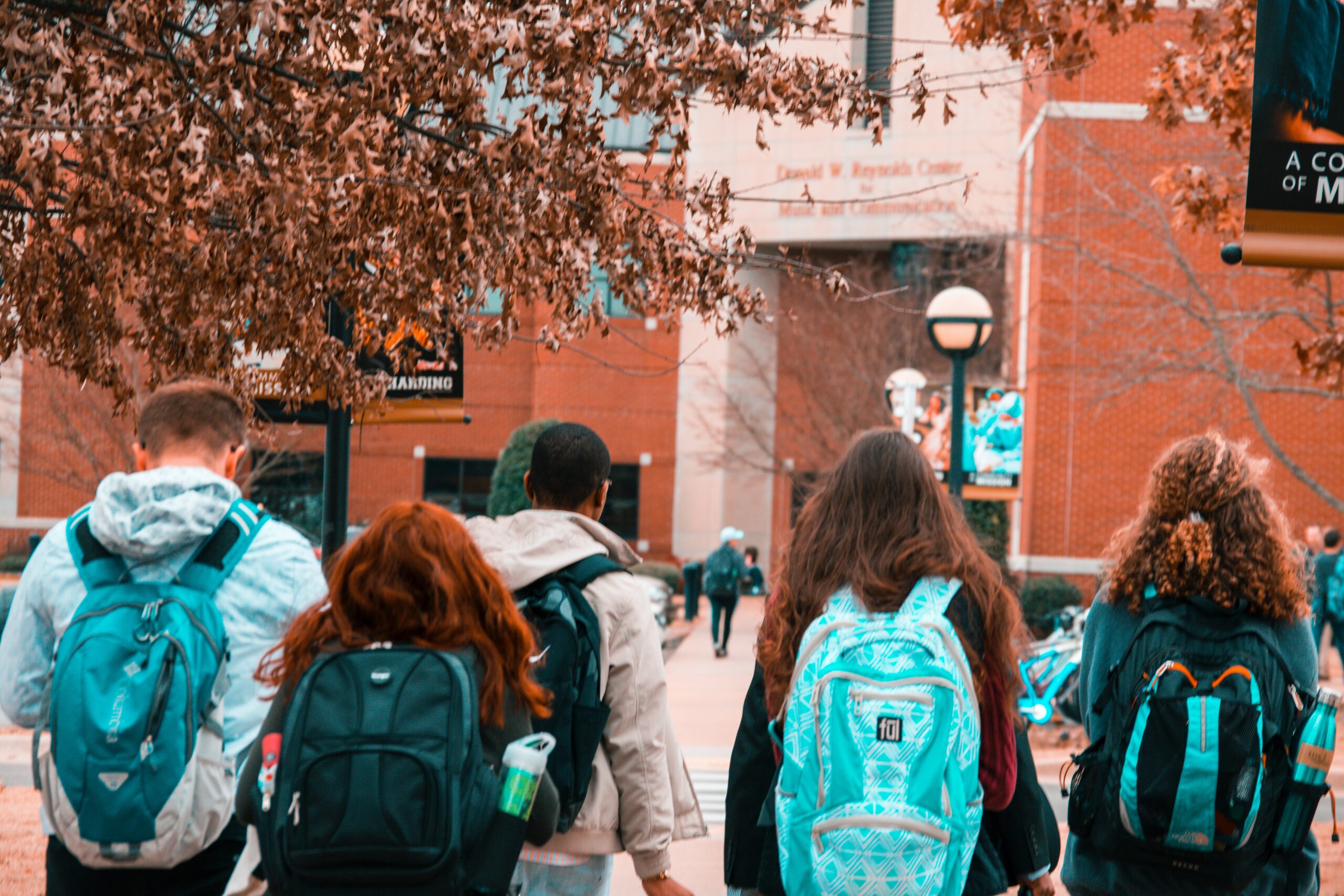 backs of students wearing backpacks walking