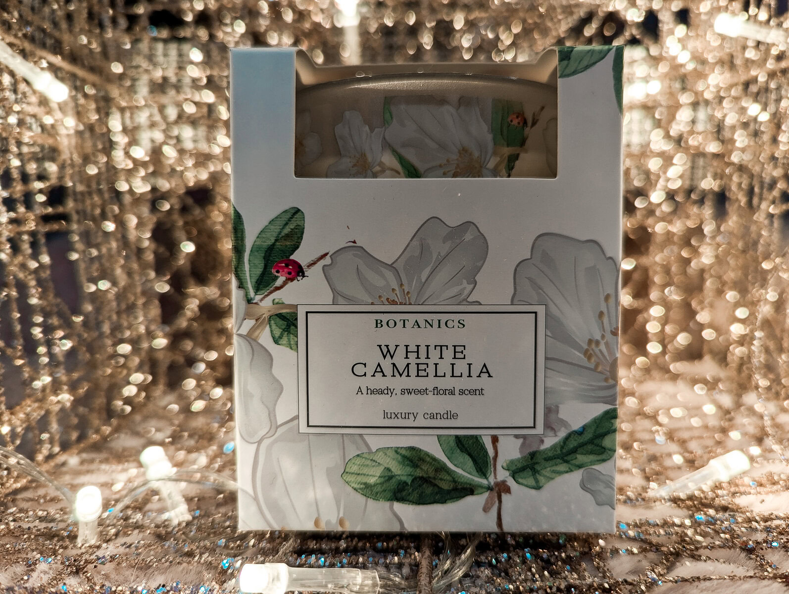the copenhagen company white camellia candle with blurred lights in the background.