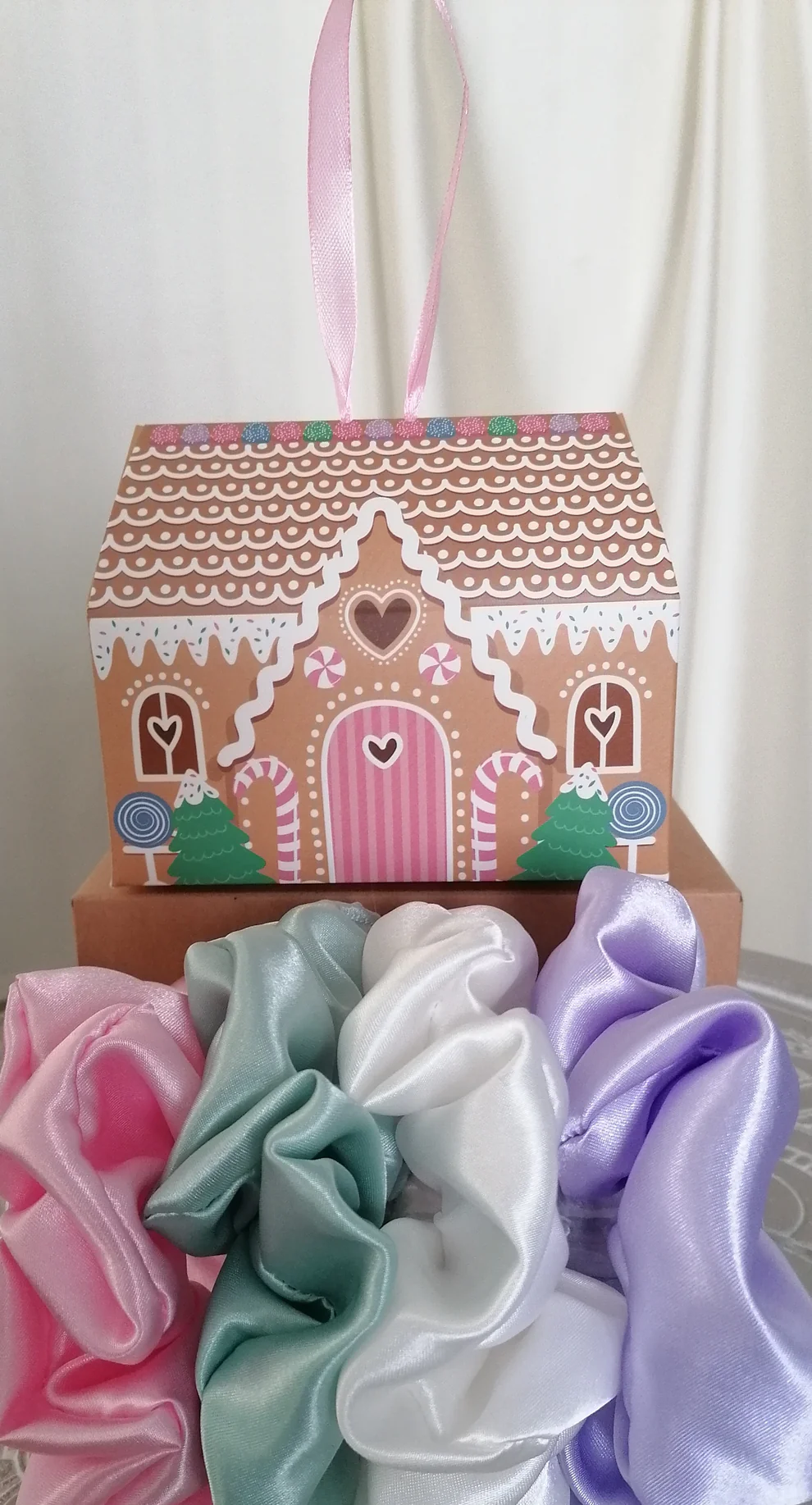 the scrunchie shed's boxed selection of schrunchies featiring a gingerbread house box and a pink, green, white and lilac crunchie in front of it