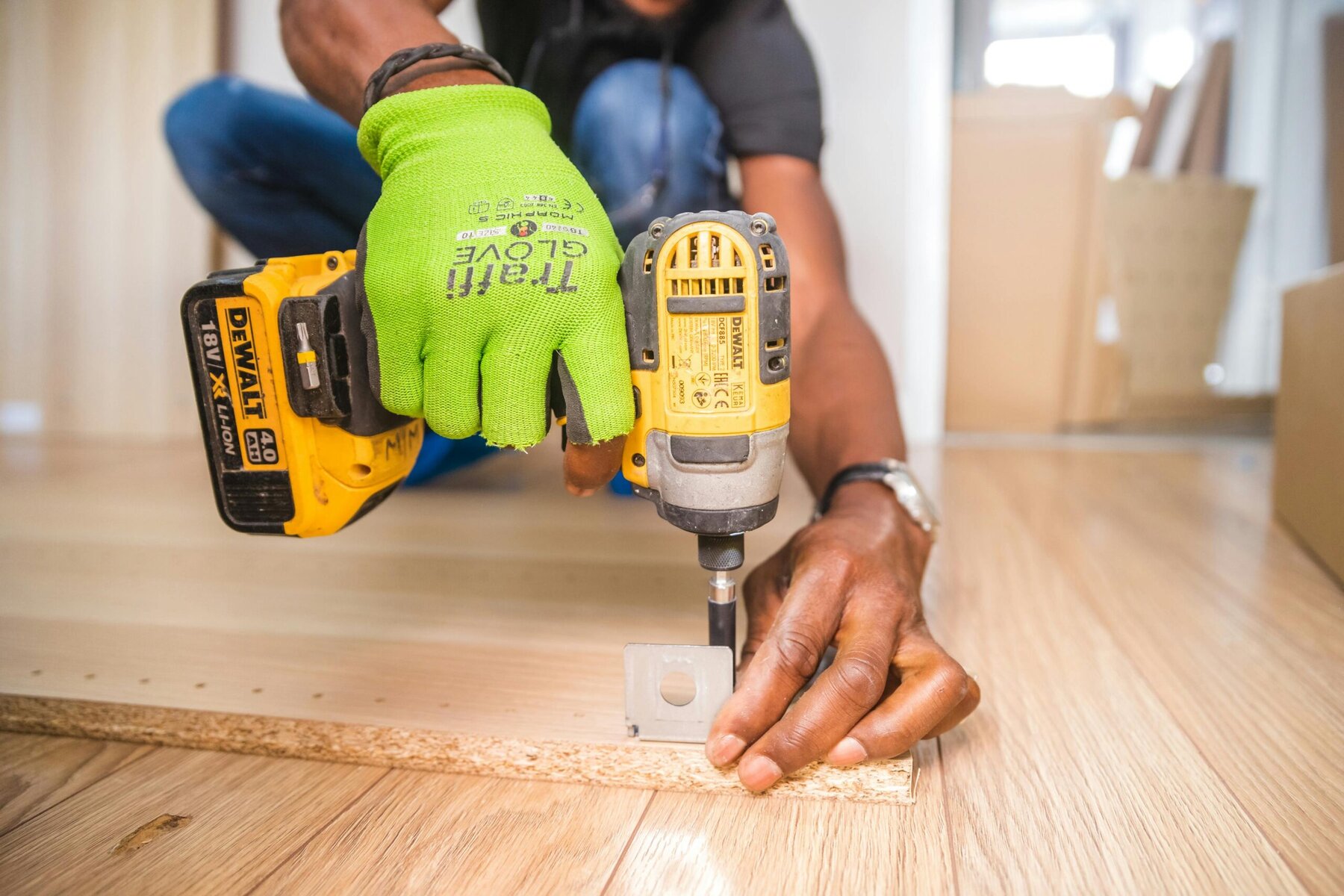 a man crouched down using a yellow drill on a piece of wood
