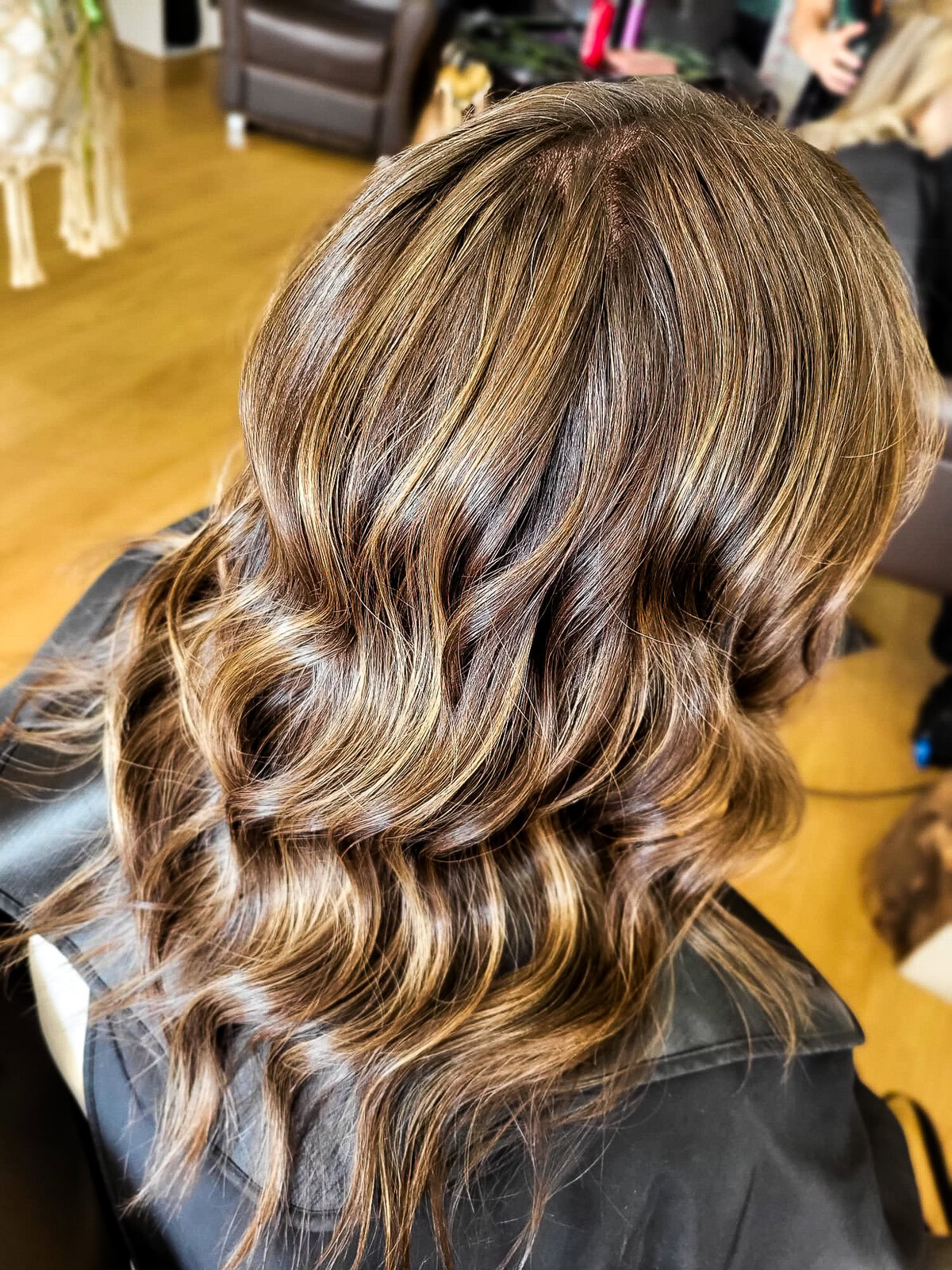 close of a womans bronw hair with low lights styled in a loose wave