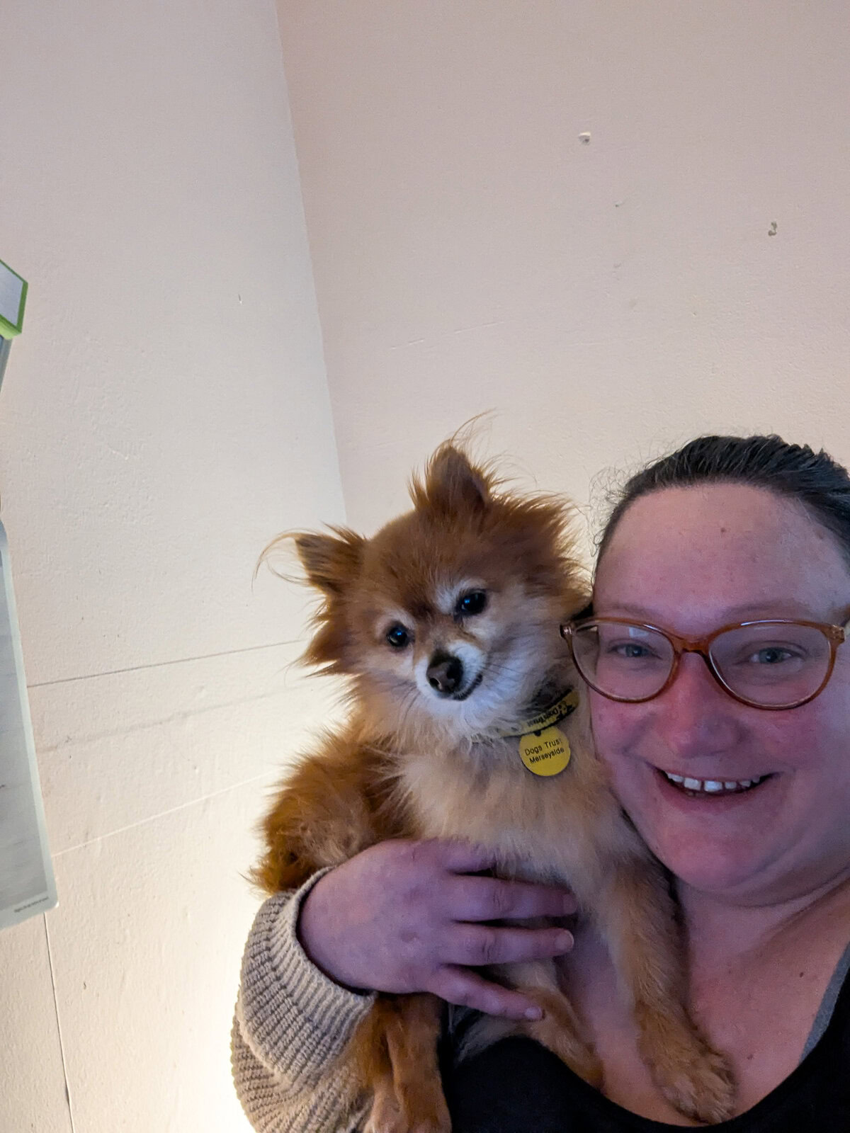 a woman with hair tired back with a tan coloured small pomeranian on her shoulder