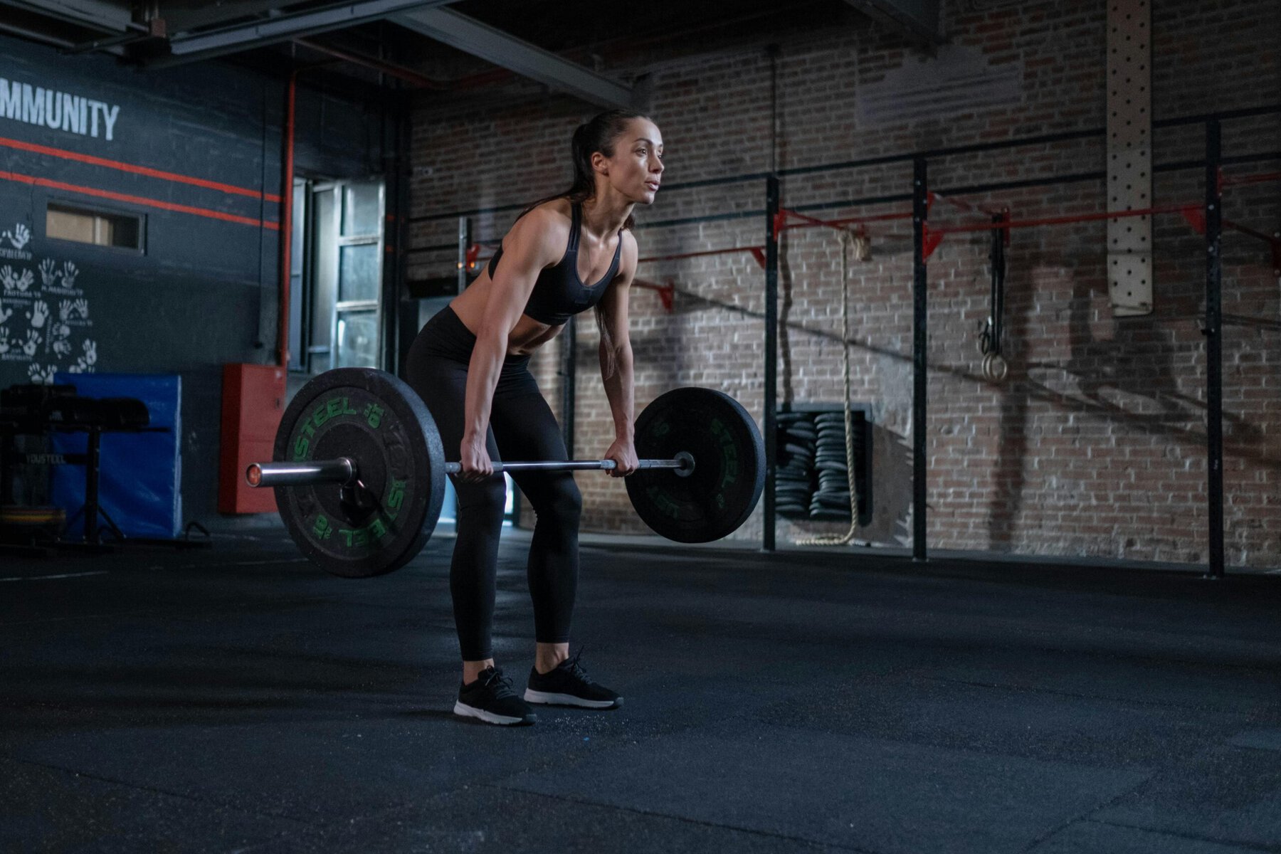 Woman in black sportswear lifting a barbell in a gym, focused on strength training
