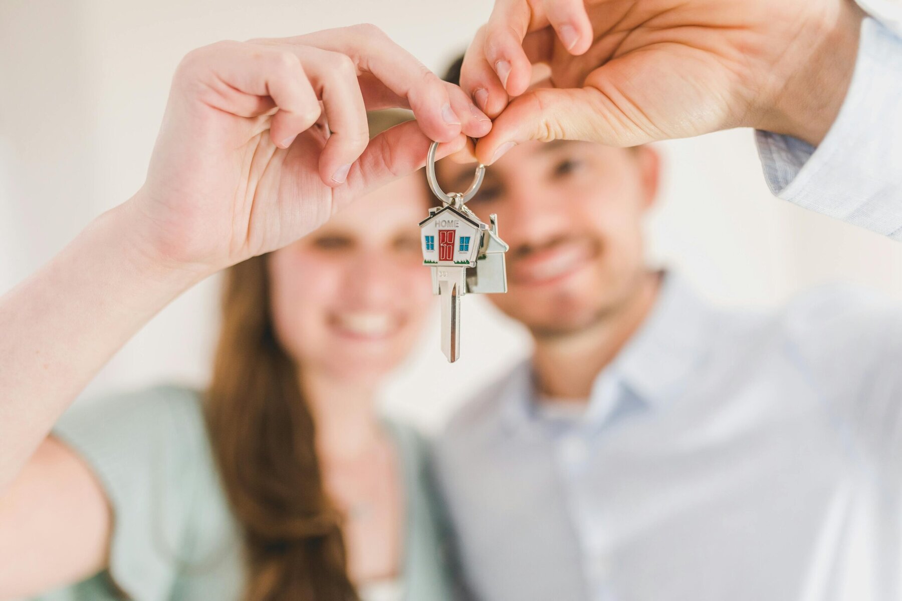 a couple in a blurred image shot holding up a house key at the camera which is the focus of the shot