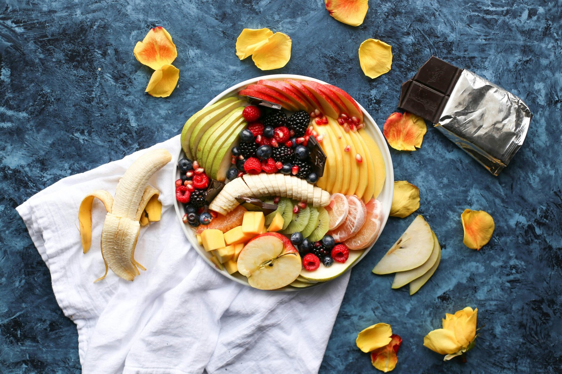 White bowl filled with a variety of sliced fresh fruit placed on a soft white textile background