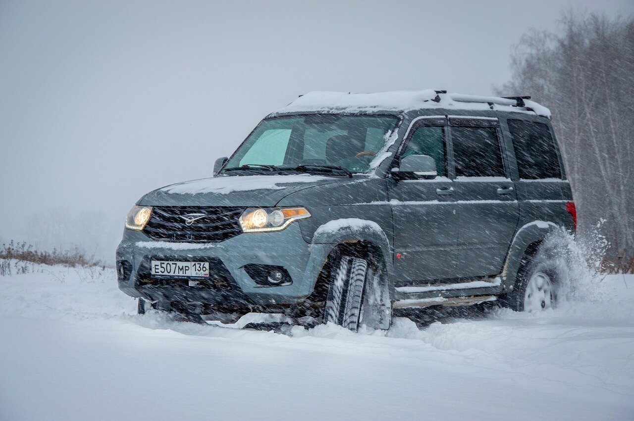 “A silver car driving through a snow-covered country road in winter, bare trees and white fields extending into the background.”