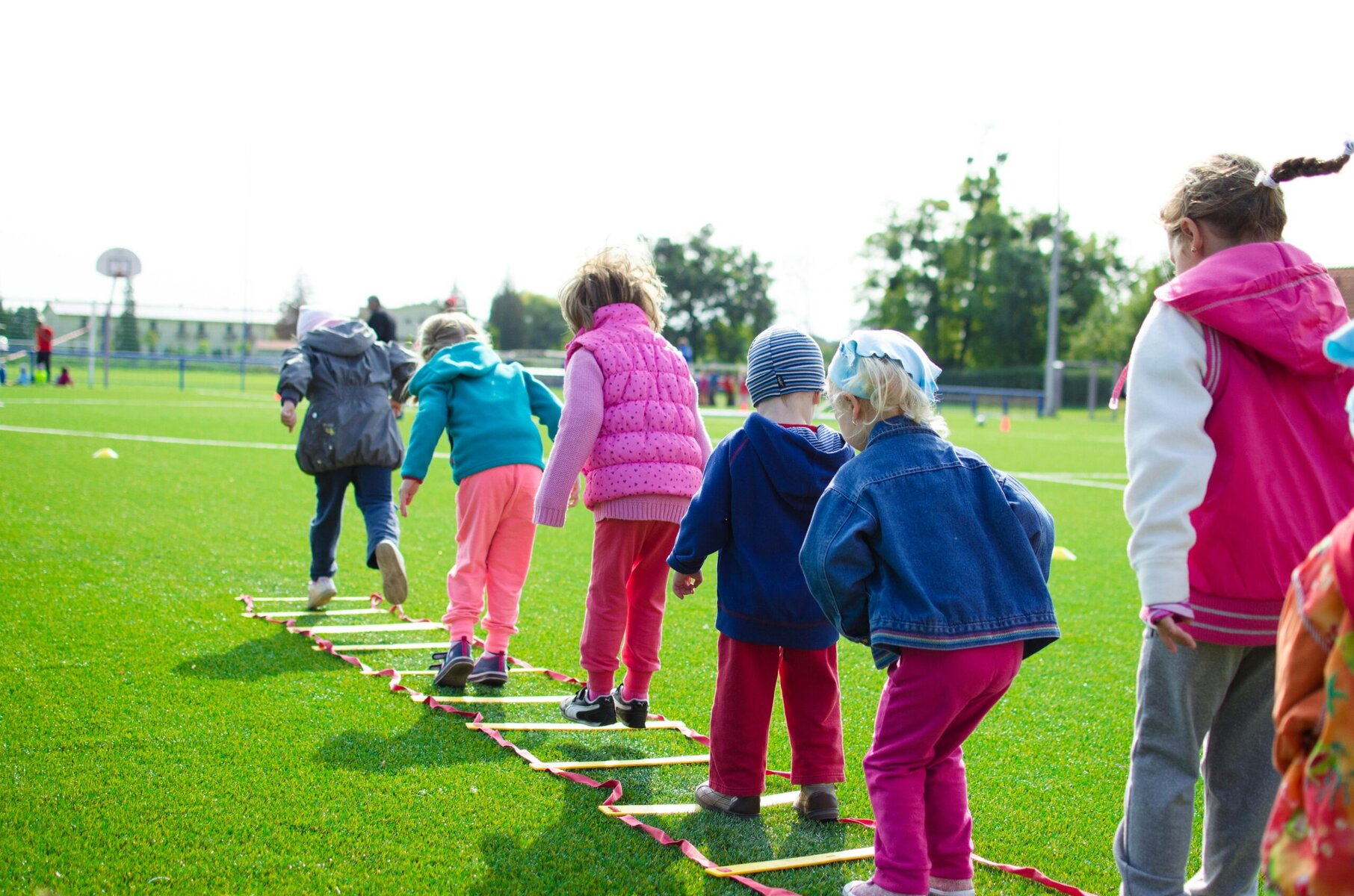 Group of children playing on a green lawn, holding hands and participating in a team-building activity outdoors.