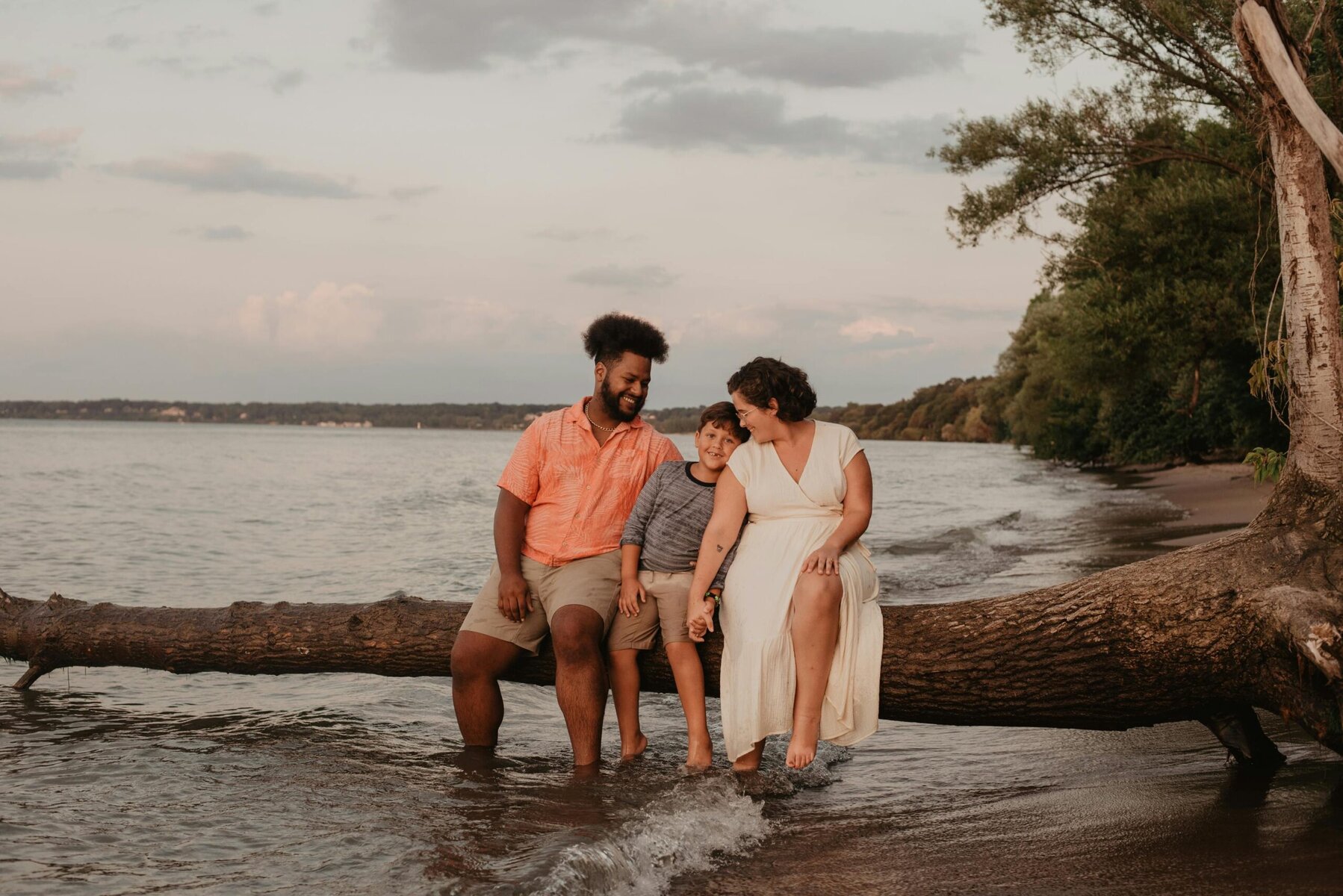 Parents sitting on a fallen tree log talking with their young son outdoors.