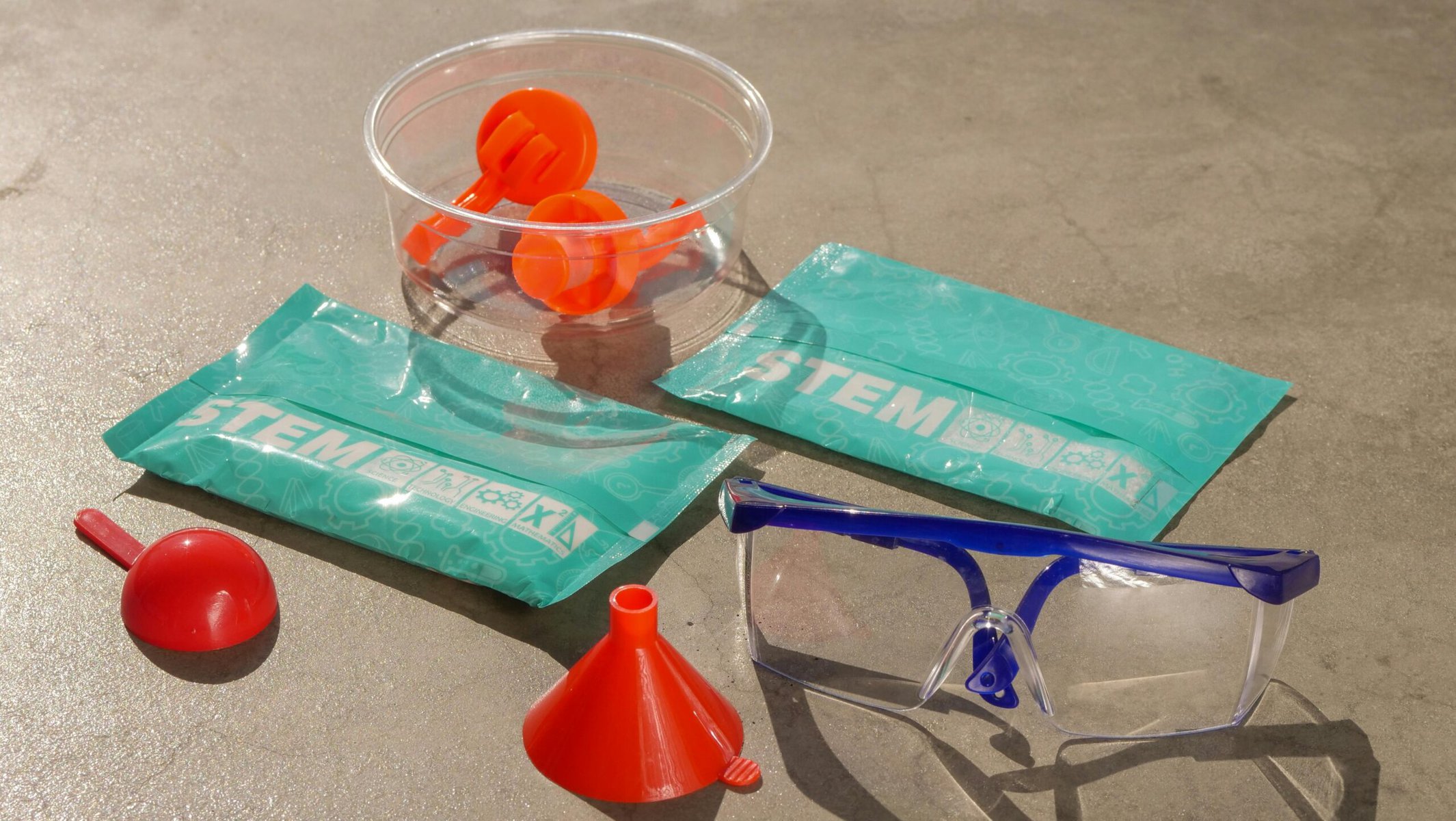 A red plastic water bottle placed next to a clear glass on a white table with blue psckets with the word STEM