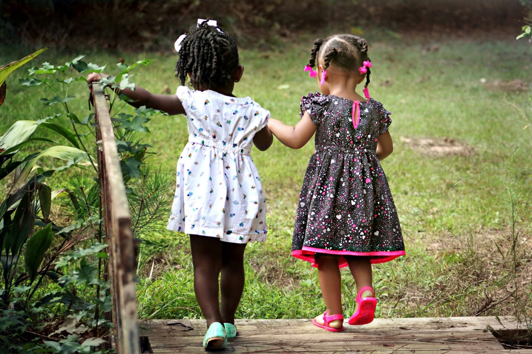Two girls walking side by side on a wooden bridge during daytime.”