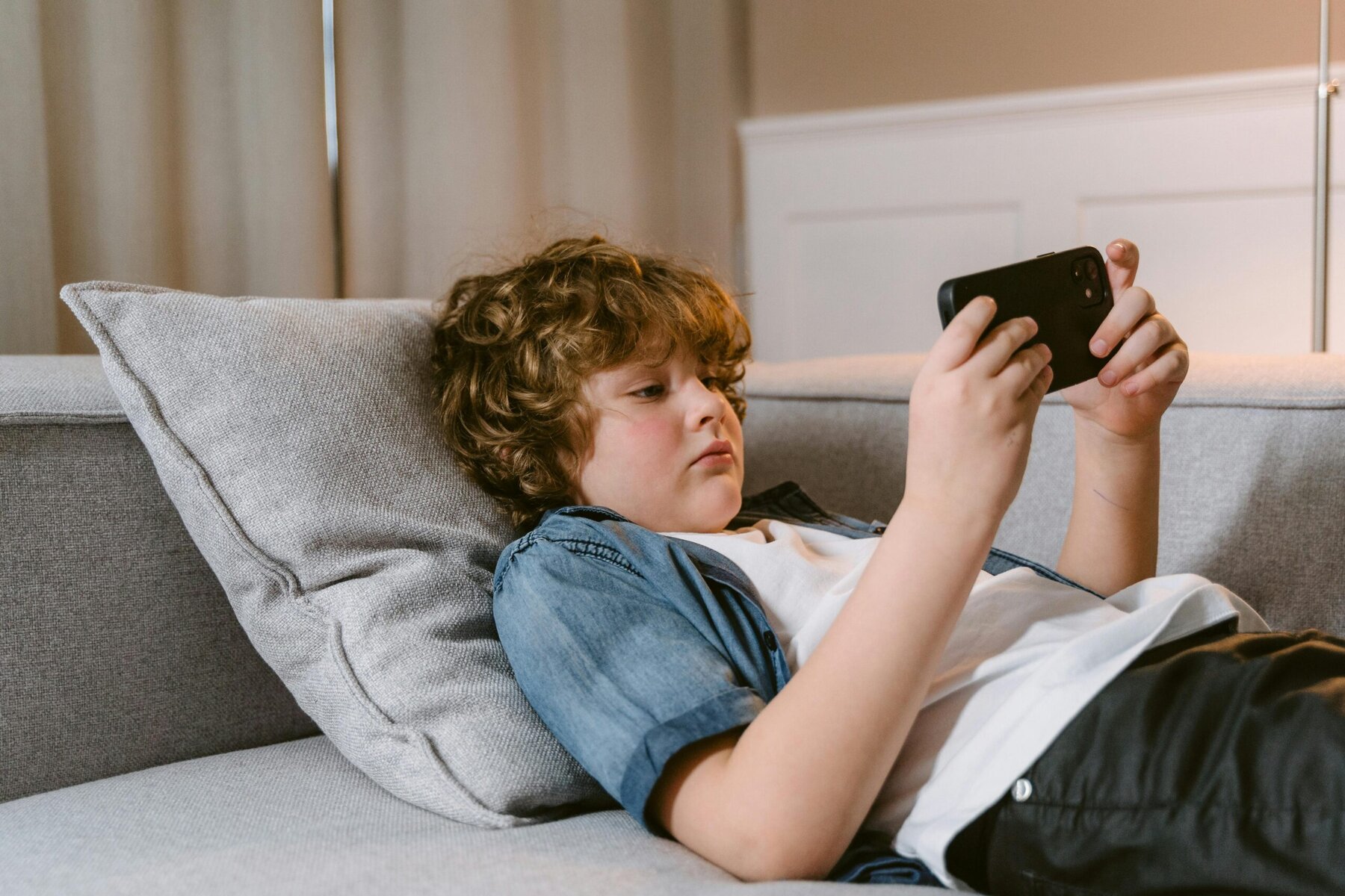 Boy lying on a sofa looking at a smartphone, indoors.