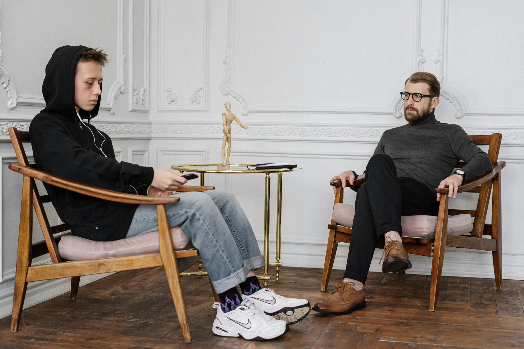 Man in black sweater and blue jeans sitting on a brown wooden chair indoors