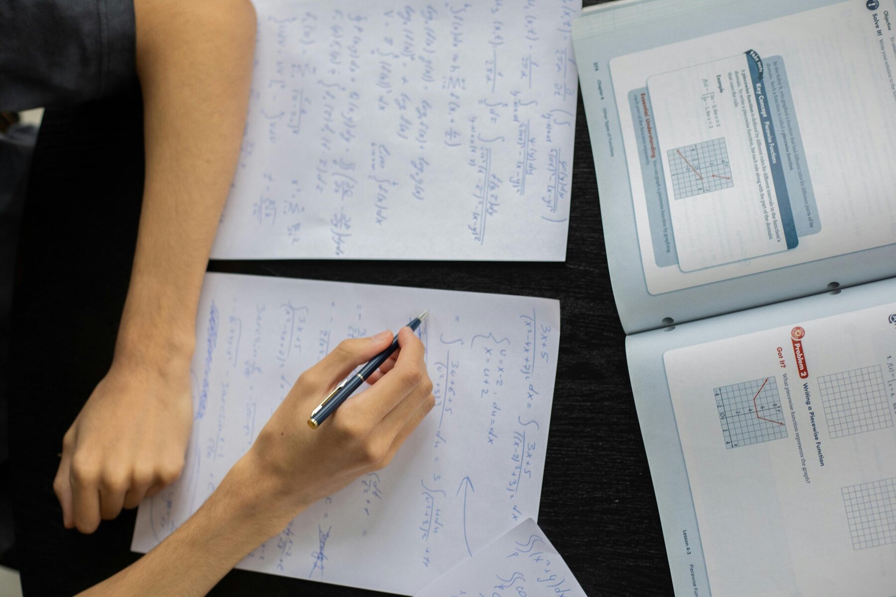 Close-up of hand writing math problems on lined paper with pen