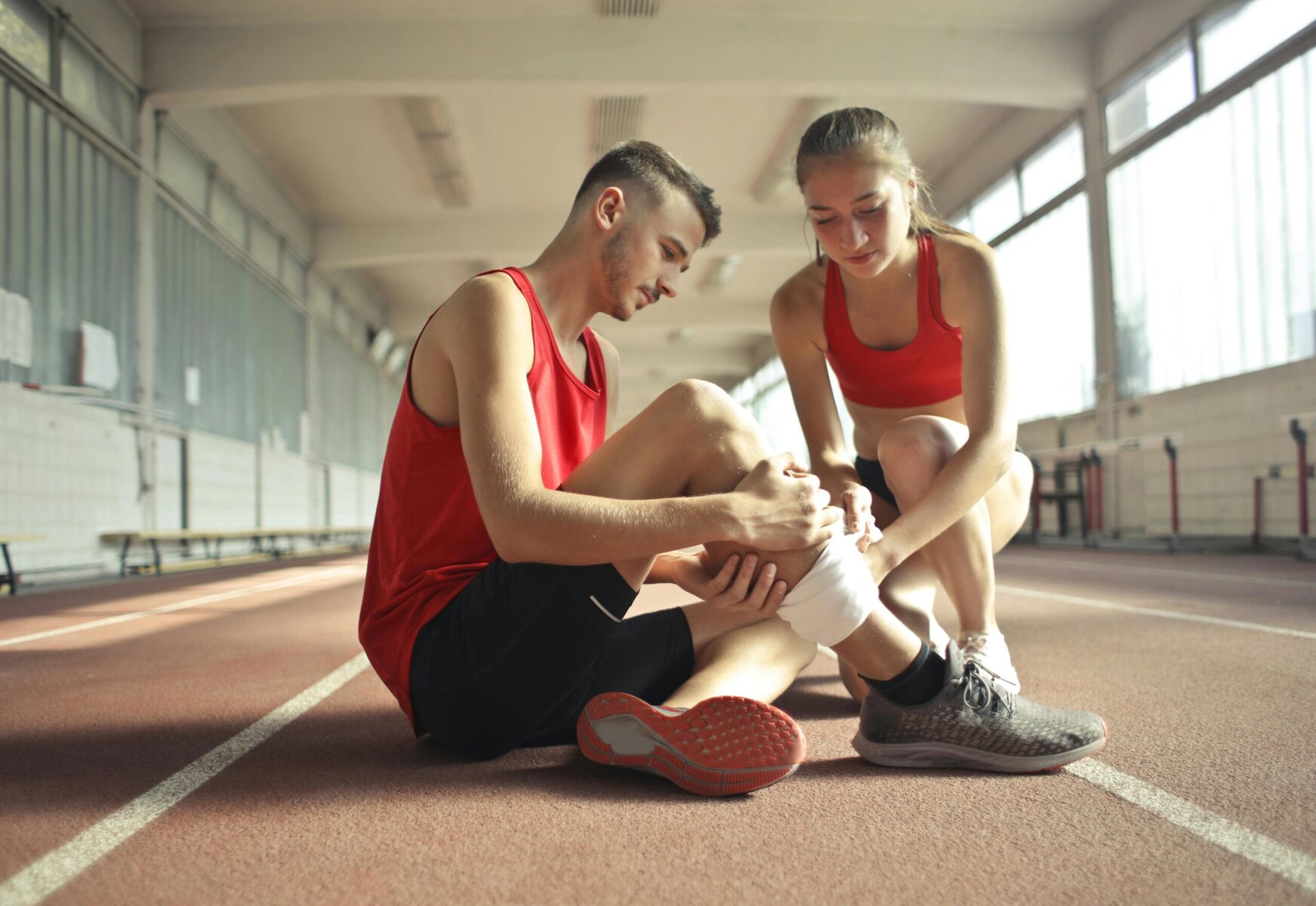 Woman wrapping an injured man’s leg with a bandage, showing support and injury care