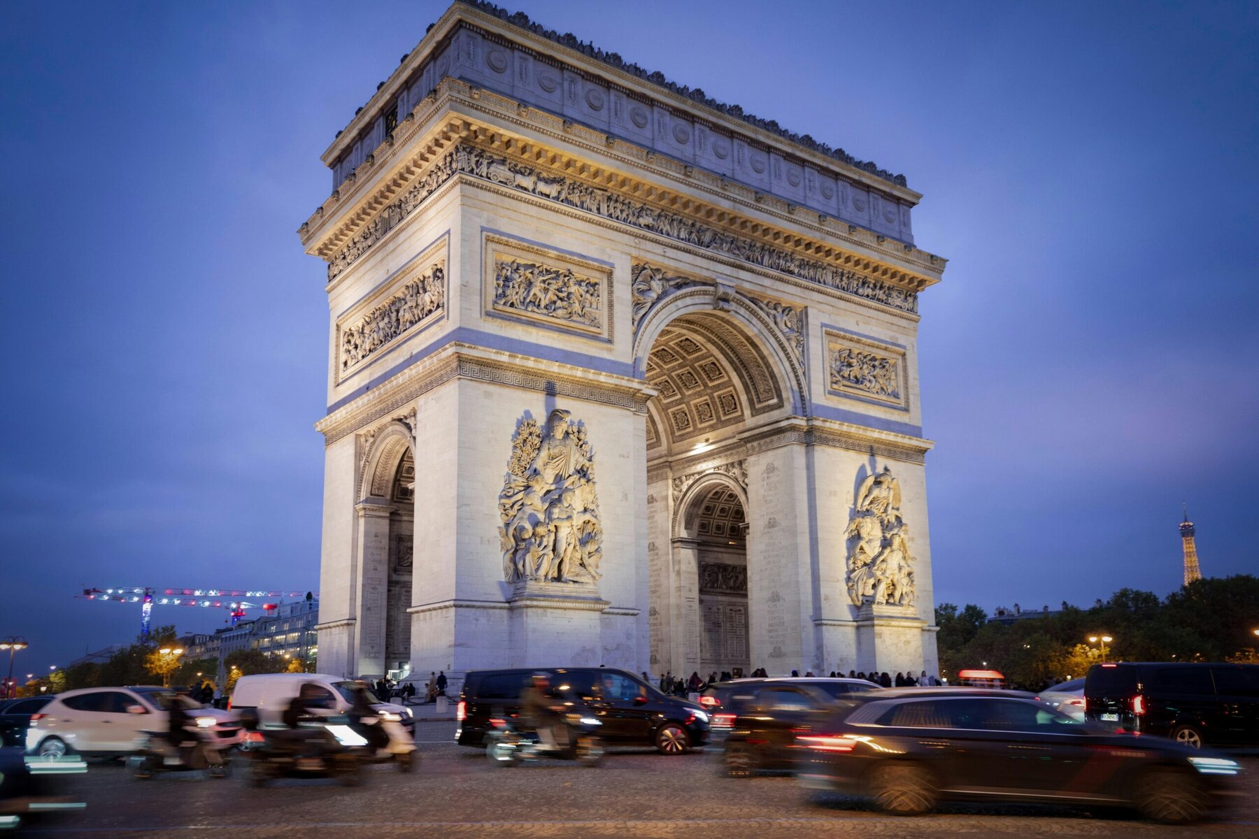 Twilight view of the illuminated Arc de Triomphe monument in Paris, France with city lights and evening sky.