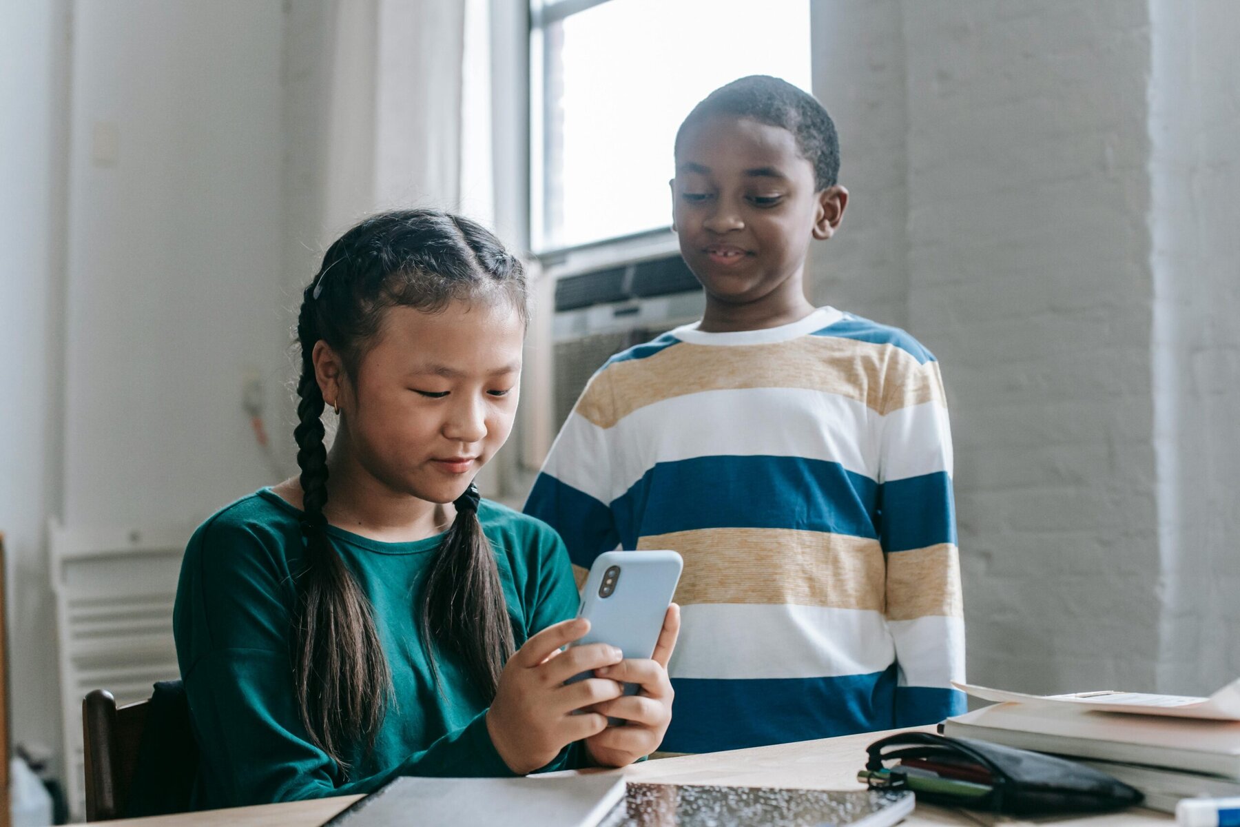 Multi-ethnic young pupils in a classroom watching a video on a smartphone together