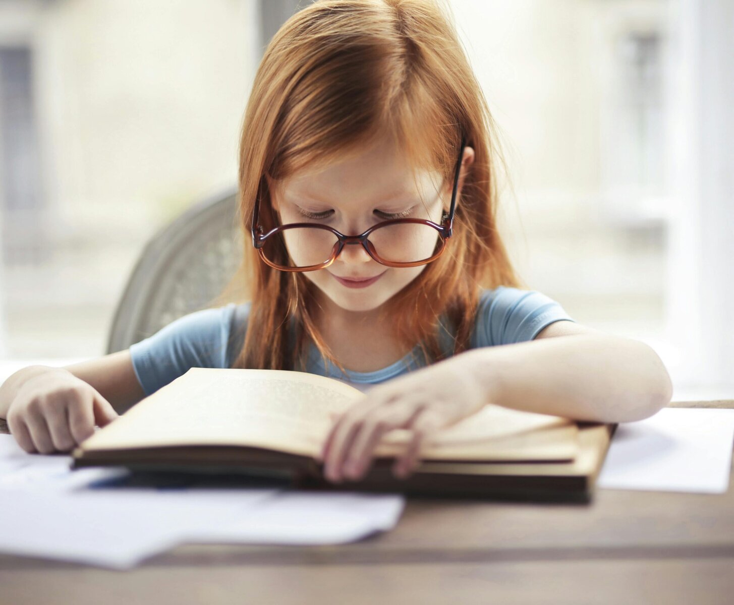 Girl in a blue long-sleeve shirt reading a book while sitting comfortably