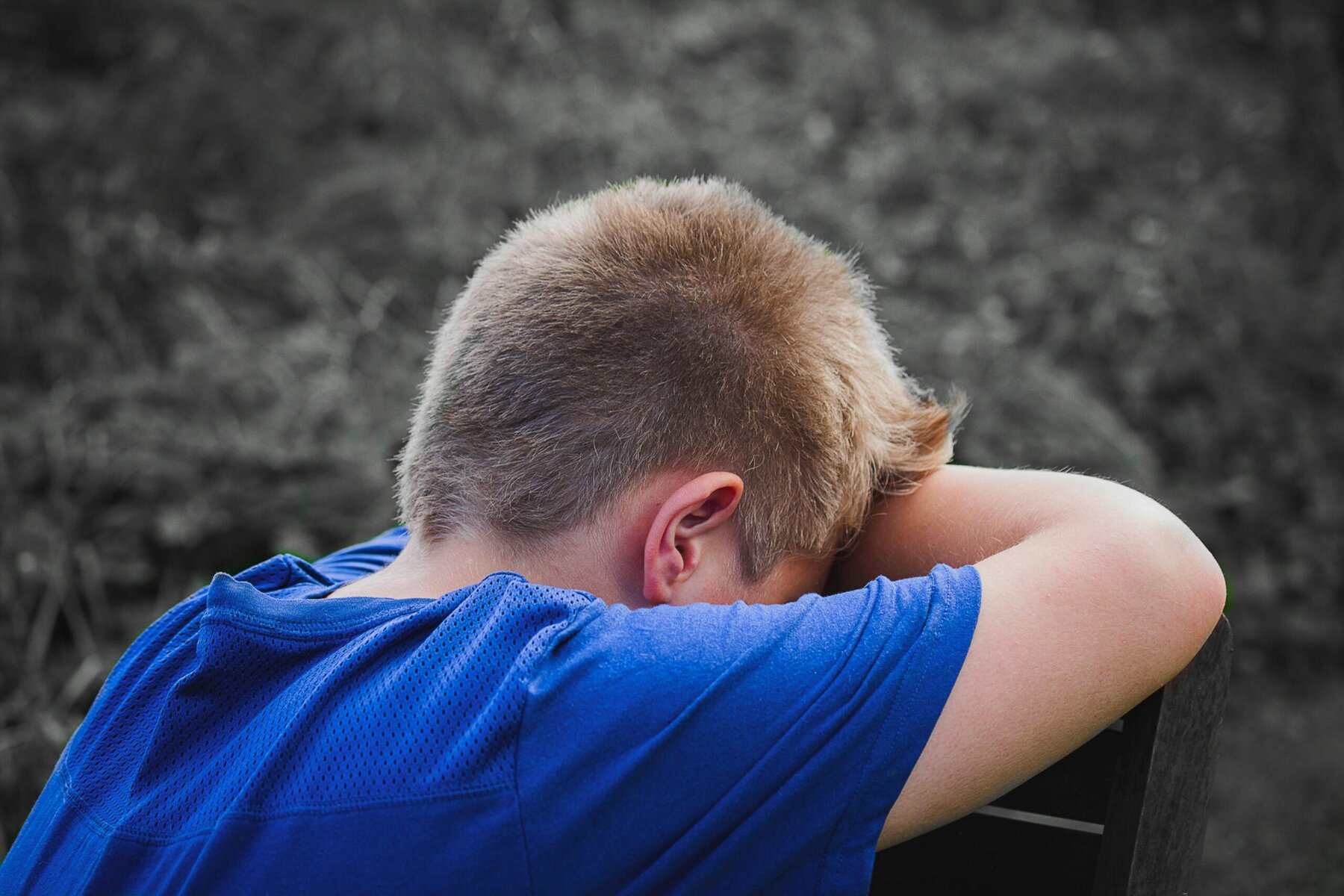 Close-up photo of a sad child leaning on a wooden chair with a thoughtful expression