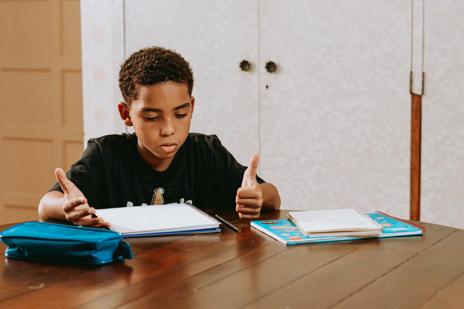 Young boy sitting at a table leaning over a workbook and learning with concentration