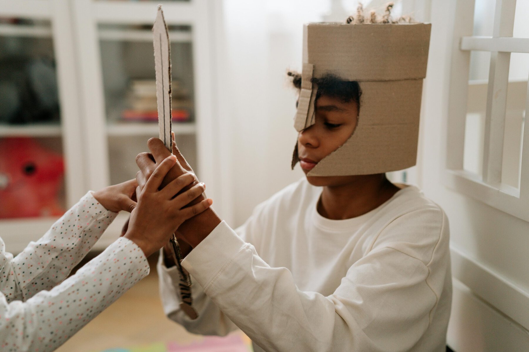 Boy in white long sleeve shirt holding a cardboard sword